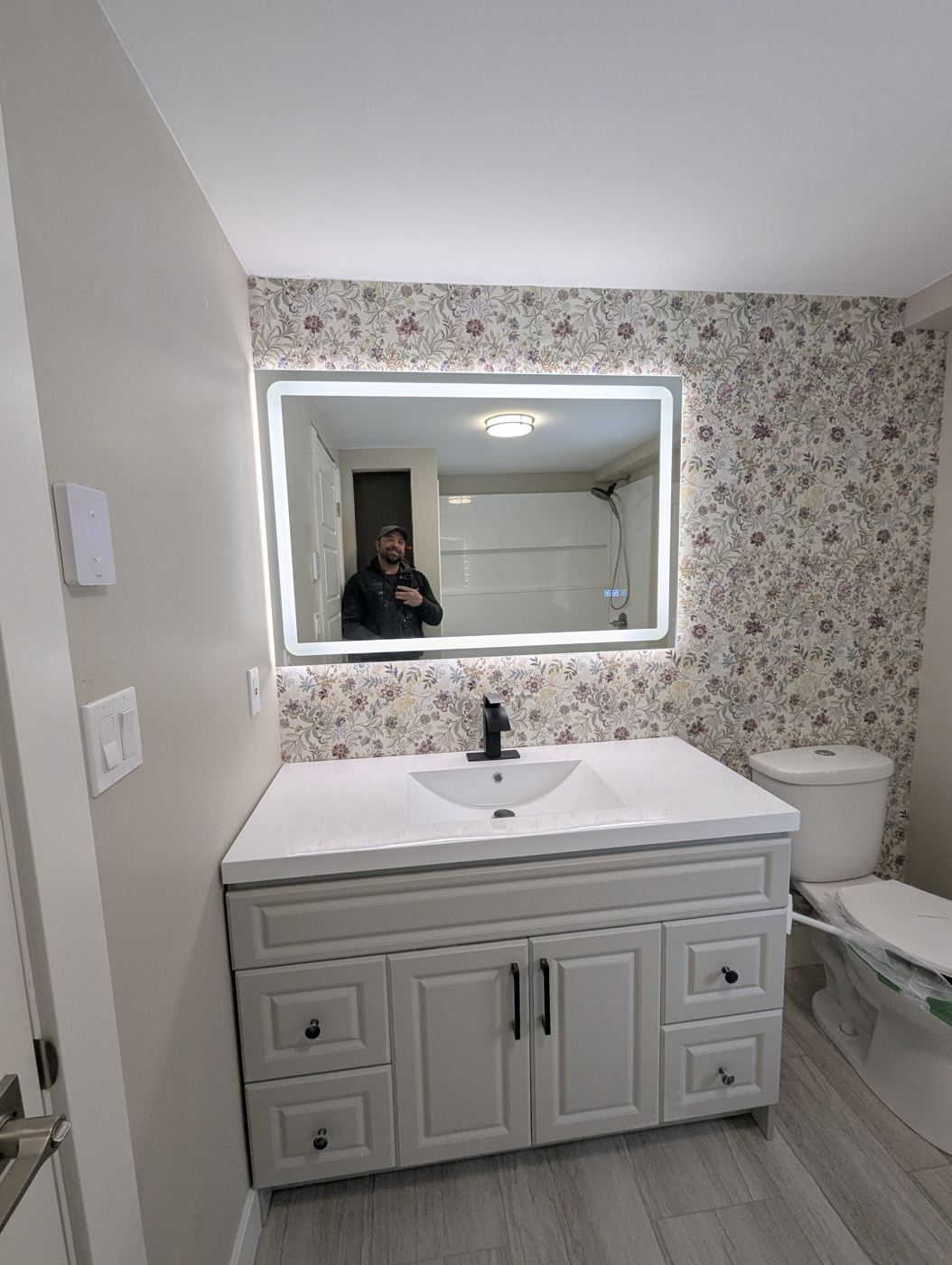 Finished bathroom vanity with backlit mirror and floral wallpaper by Valhalla Construction