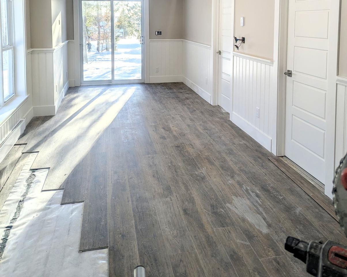 Finished living room with plank flooring and custom white wainscoting by Valhalla Construction