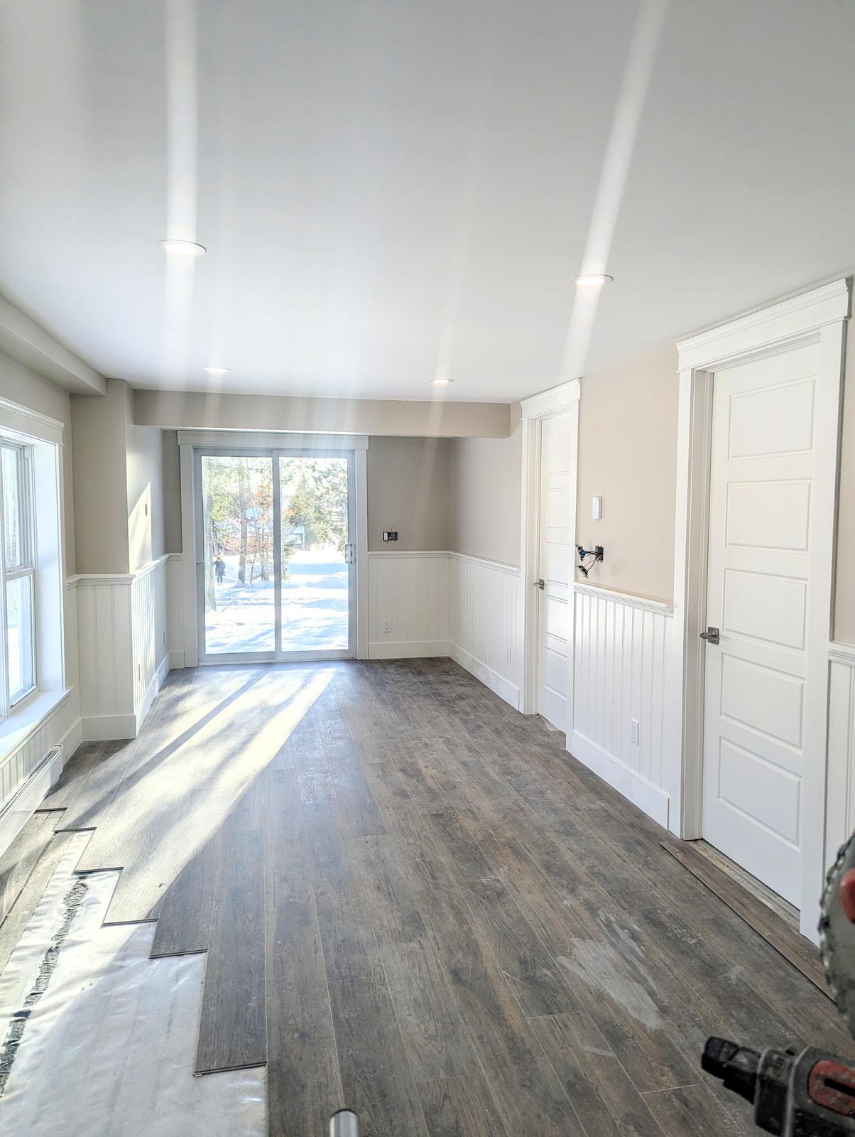 Finished living room with plank flooring and custom white wainscoting by Valhalla Construction