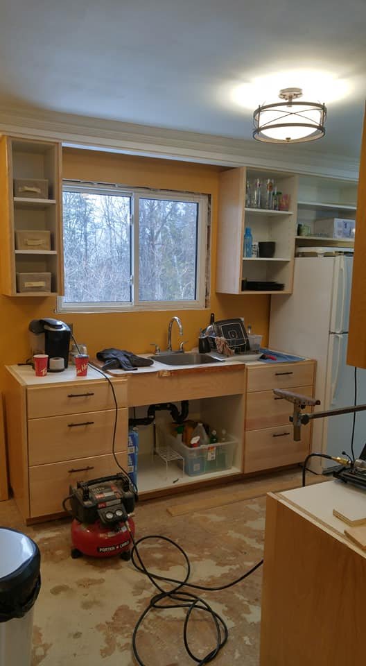 Hand-built honey oak kitchen cabinets and open shelving installed around a corner window, in progress