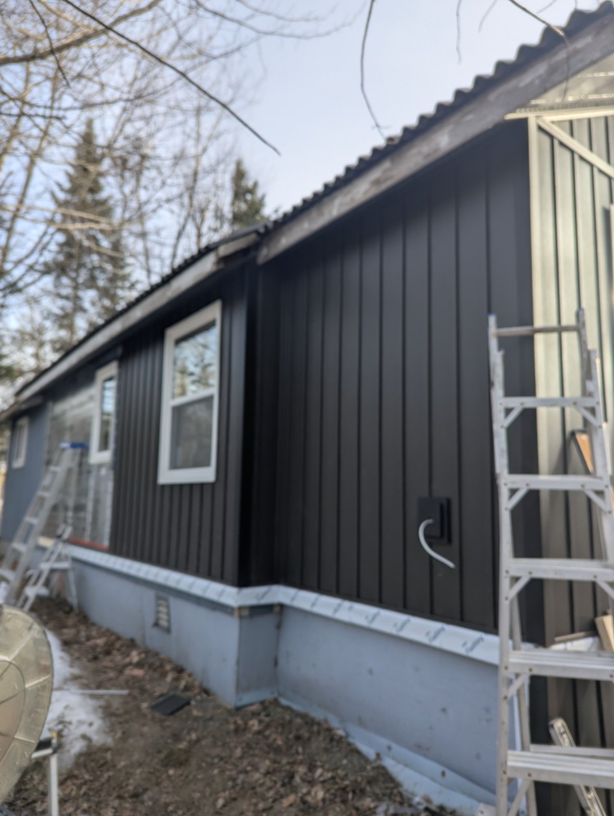 Completed black vertical board-and-batten steel siding with white window trim by Valhalla Construction